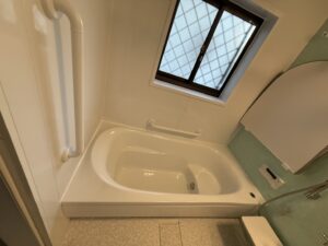 施工後の浴室の写真　右側一面だけ淡い緑色の壁　出入口に手すりがついている
