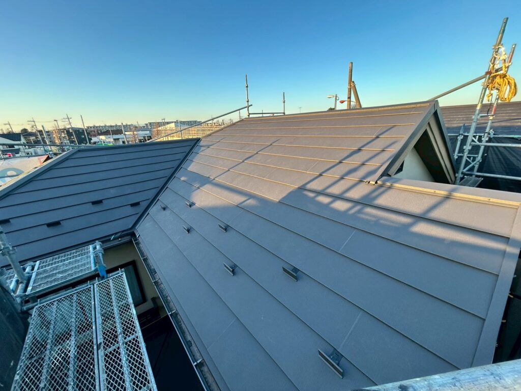 屋根上葺き工事の施工後の写真 屋根の真横の足場から撮った写真である 左側へL字の伸びる茶色の屋根