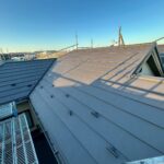 屋根上葺き工事の施工後の写真　屋根の真横の足場から撮った写真である　左側へL字の伸びる茶色の屋根